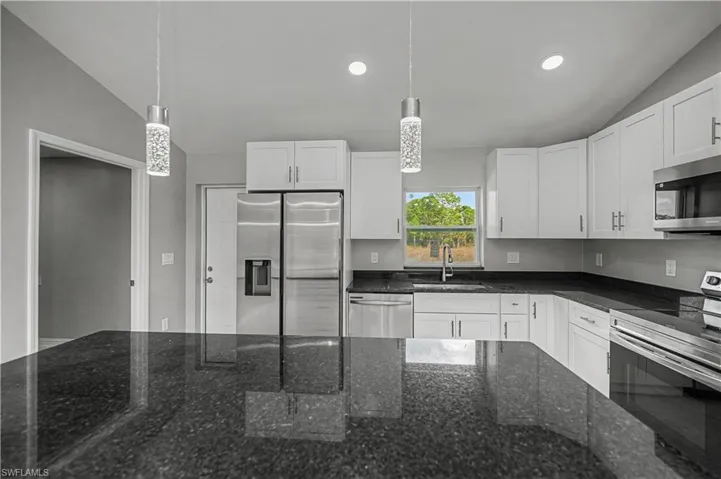 Kitchen featuring appliances with stainless steel finishes, white cabinetry, dark stone countertops, hanging light fixtures, and vaulted ceiling