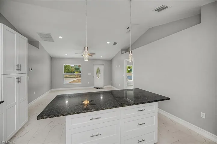 Kitchen with white cabinets, light marble finish flooring, dark stone countertops, a center island, and vaulted ceiling