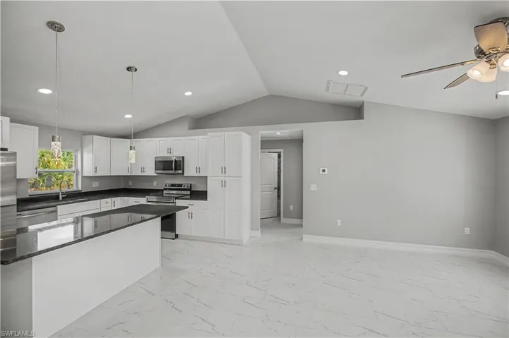 Kitchen featuring hanging light fixtures, appliances with stainless steel finishes, white cabinetry, dark stone countertops, and vaulted ceiling