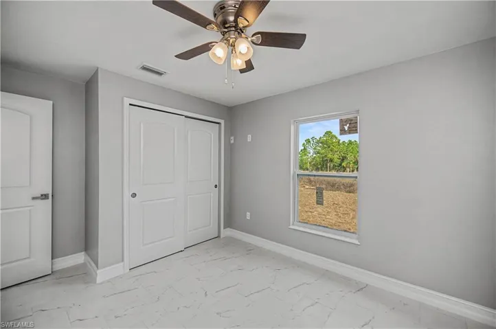 Unfurnished bedroom with ceiling fan, a closet, and light marble finish flooring