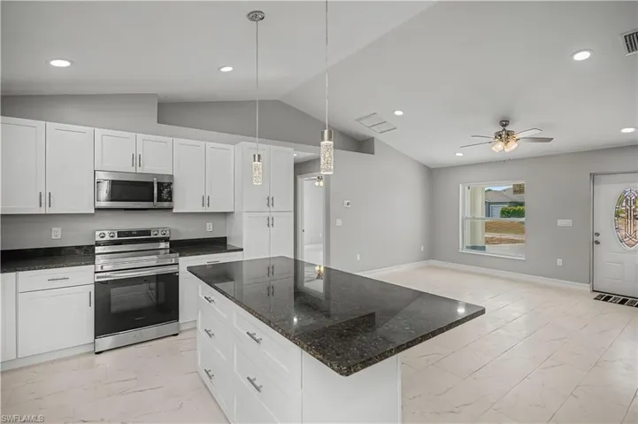 Kitchen featuring appliances with stainless steel finishes, light marble finish flooring, hanging light fixtures, dark stone countertops, and a kitchen island