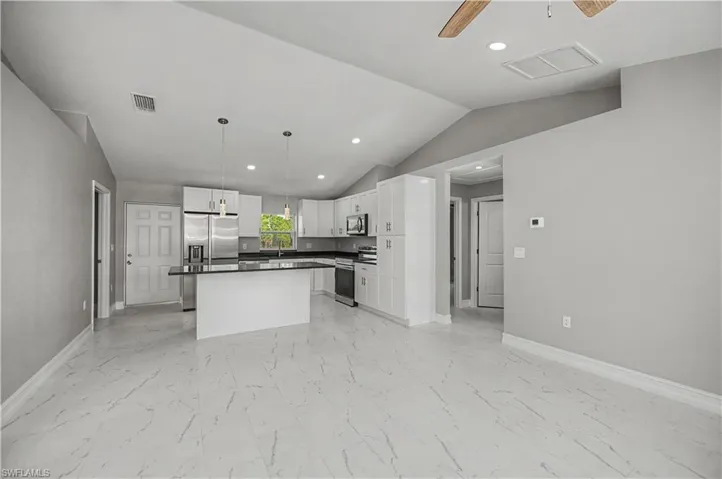 Kitchen featuring appliances with stainless steel finishes, pendant lighting, light marble finish floors, dark countertops, and lofted ceiling