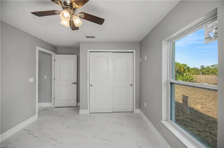 Unfurnished bedroom with light marble finish floors, ceiling fan, and a closet