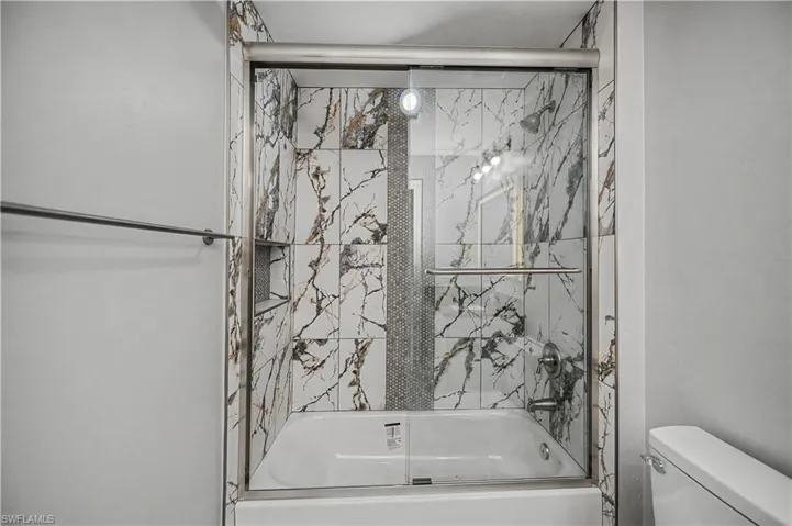 Full bath featuring combined bath / shower with glass door and toilet