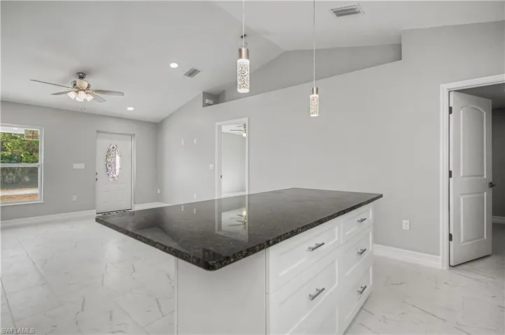 Kitchen featuring light marble finish flooring, white cabinetry, dark stone counters, decorative light fixtures, and lofted ceiling