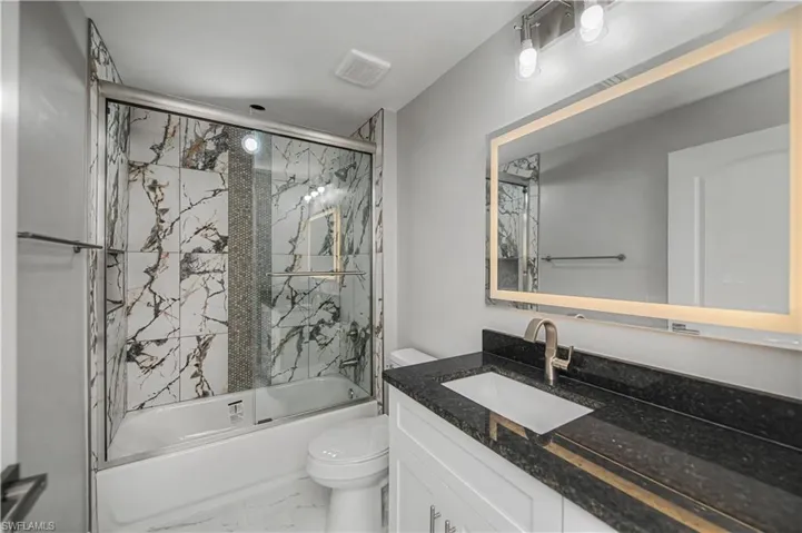 Bathroom featuring enclosed tub / shower combo, vanity, and marble look tiles