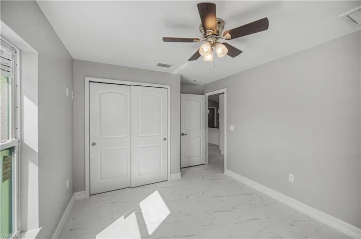 Unfurnished bedroom featuring light marble finish floors, ceiling fan, and a closet