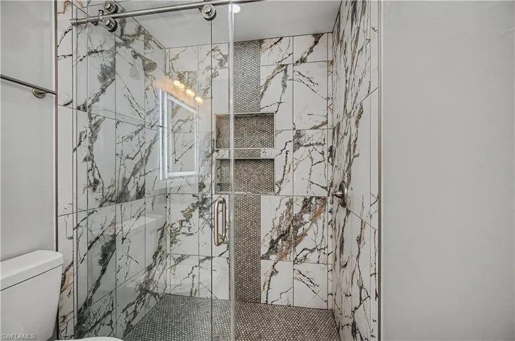 Full bath with a marble finish shower and toilet
