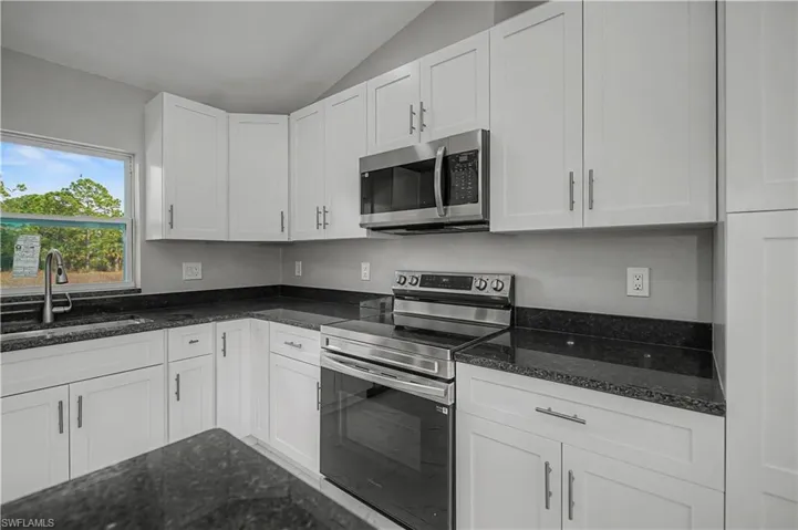 Kitchen featuring appliances with stainless steel finishes, white cabinetry, dark stone counters, and lofted ceiling