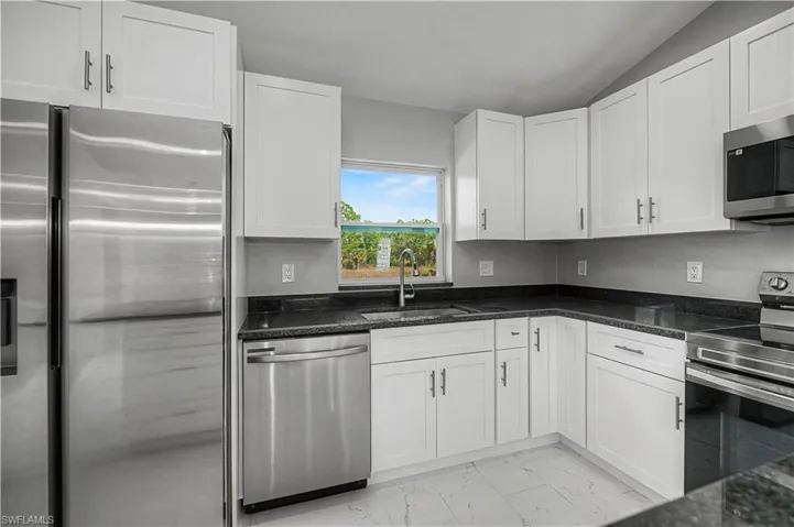 Kitchen with appliances with stainless steel finishes, white cabinets, light marble finish flooring, dark stone countertops, and vaulted ceiling