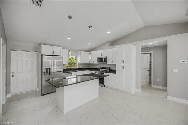 Kitchen featuring appliances with stainless steel finishes, decorative light fixtures, vaulted ceiling, a kitchen island, and dark stone counters