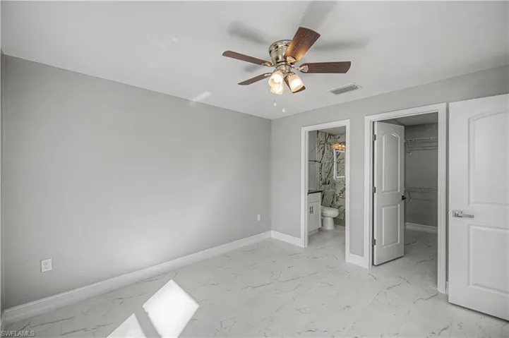 Unfurnished bedroom with a walk in closet, ceiling fan, and light marble finish floors