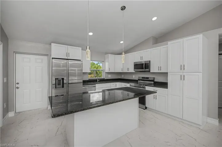 Kitchen featuring dark stone counters, appliances with stainless steel finishes, vaulted ceiling, white cabinetry, and recessed lighting