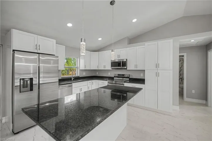 Kitchen featuring dark stone countertops, white cabinets, stainless steel appliances, vaulted ceiling, and decorative light fixtures