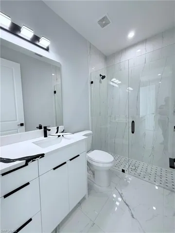 Bathroom featuring vanity, a shower with shower door, and toilet