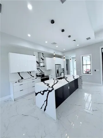 Kitchen with appliances with stainless steel finishes, exhaust hood, a large island with sink, pendant lighting, and white cabinetry