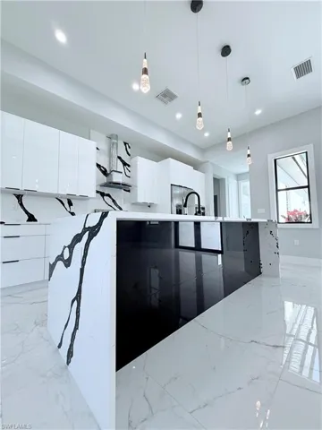 Kitchen with light stone counters, white cabinetry, hanging light fixtures, and stainless steel refrigerator with ice dispenser