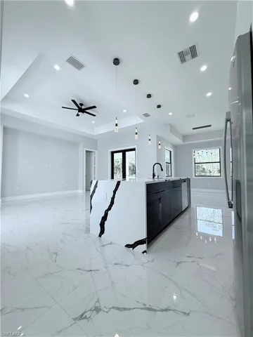 Kitchen with hanging light fixtures, a tray ceiling, stainless steel refrigerator, and a wealth of natural light