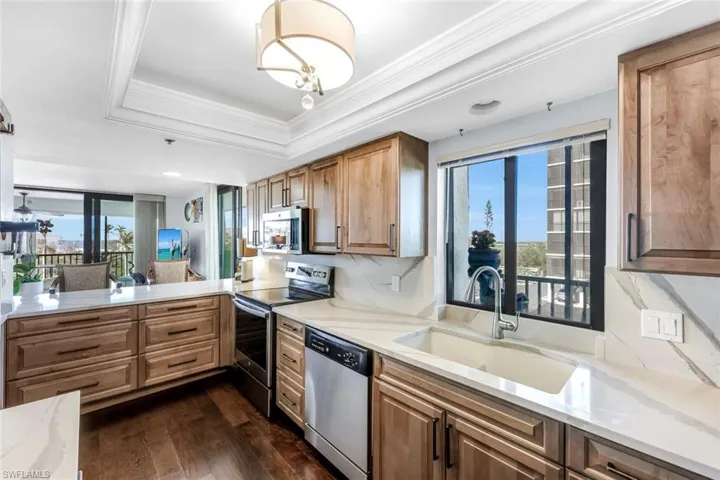 Kitchen featuring stainless steel appliances, light stone countertops, dark wood finished floors, crown molding, and a raised ceiling