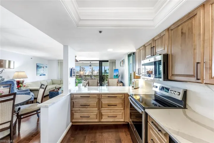 Kitchen featuring open floor plan, appliances with stainless steel finishes, a peninsula, light stone counters, and dark wood-style flooring