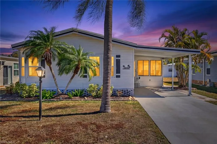 The property features a white exterior with dark shutters, a covered carport, and a well-maintained lawn