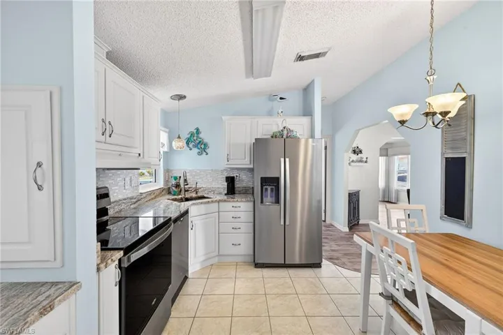 Kitchen with stainless steel appliances, white cabinets, light stone countertops, and arched walkways