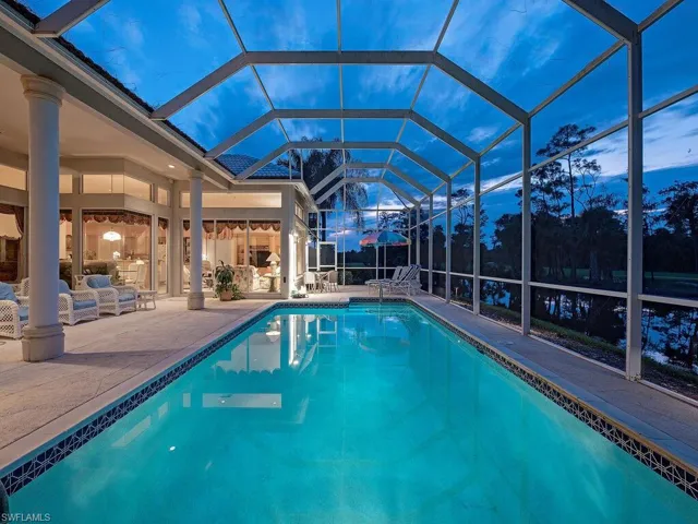 Pool at dusk with glass enclosure and a patio area