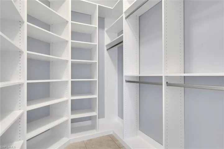 Walk-in closet featuring extensive white shelving, multiple hanging rods, and light-toned tile flooring