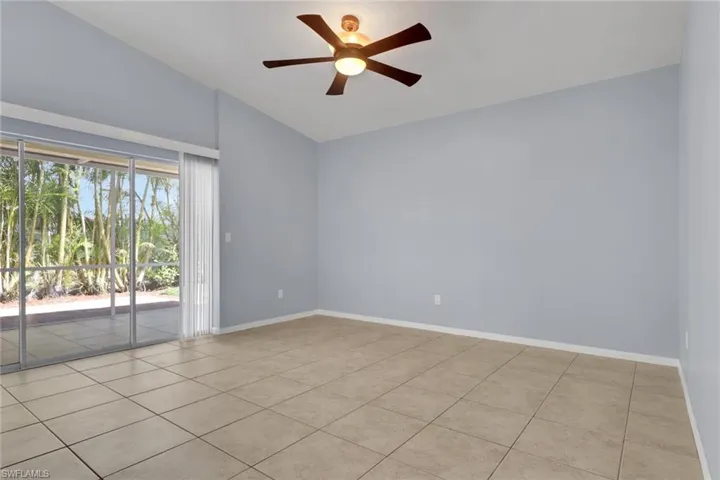 Spacious room featuring vaulted ceilings, a ceiling fan with integrated lighting, and large sliding glass doors opening to an outdoor patio with surrounding foliage