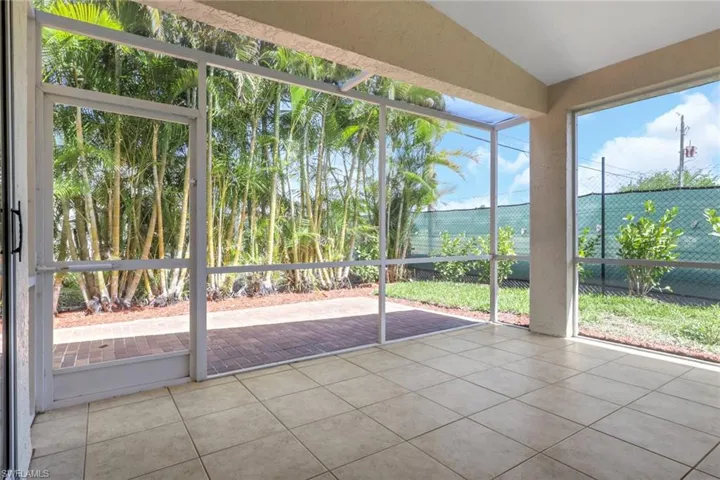 Screened lanai featuring neutral tile flooring, a patio area with brick pavers, and established tropical landscaping