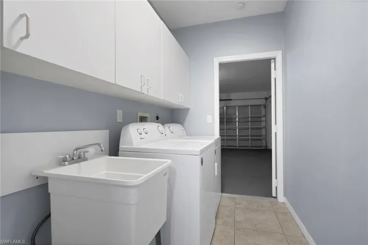 Dedicated laundry area featuring white upper cabinetry, a utility sink with a chrome faucet, and neutral-toned tile flooring