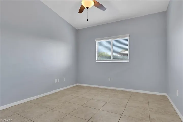 Spacious room featuring neutral tone tile flooring, light gray walls, and a window with blinds