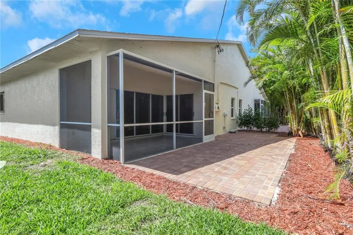 Screened patio with paver flooring, bordered by a textured stucco exterior and a manicured lawn