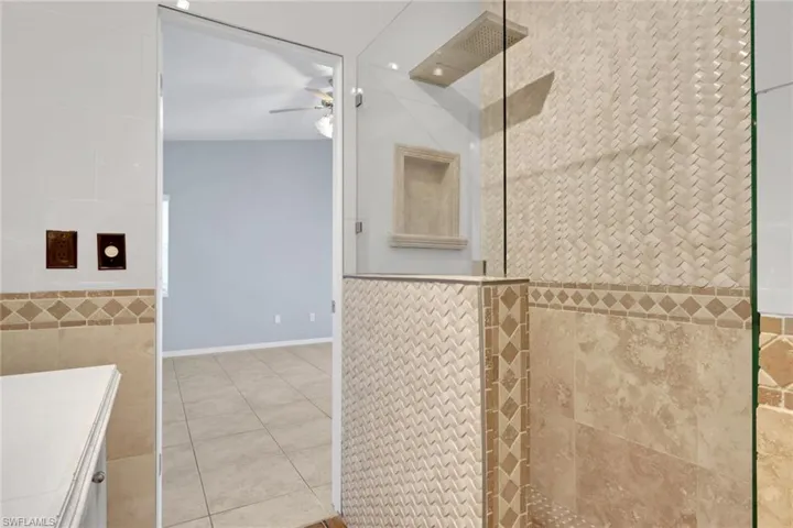 Tiled shower enclosure featuring a glass partition, geometric accent tile, a recessed niche, and a ceiling-mounted rainfall showerhead