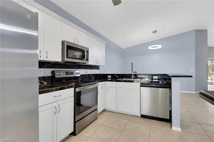 Kitchen featuring white cabinetry, stainless steel appliances, black countertops with white veining, and tile flooring