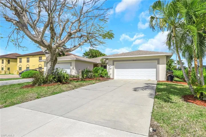 Exterior stucco residence with an attached garage, featuring a concrete driveway, mature palm trees, and established landscaping