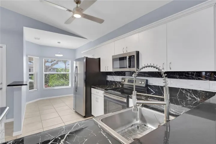 Kitchen featuring black marbled countertops, white upper and lower cabinetry, stainless steel appliances, a stainless steel sink with a gooseneck faucet, and a breakfast nook with bay windows