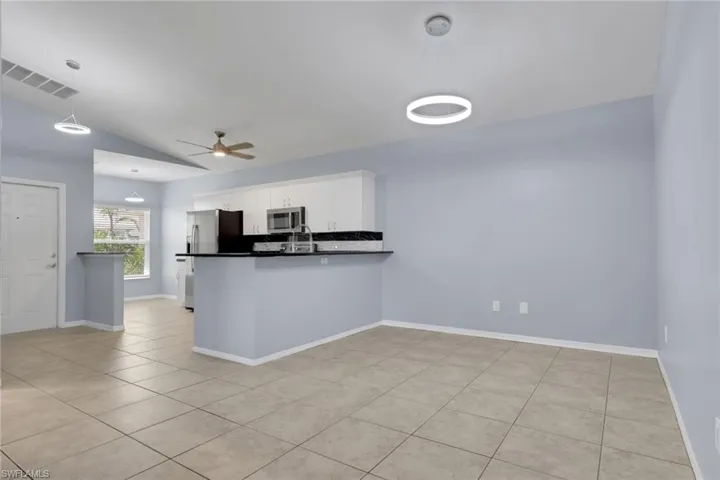 Spacious open-concept living area featuring a kitchen with white cabinetry, dark countertops, and stainless steel appliances