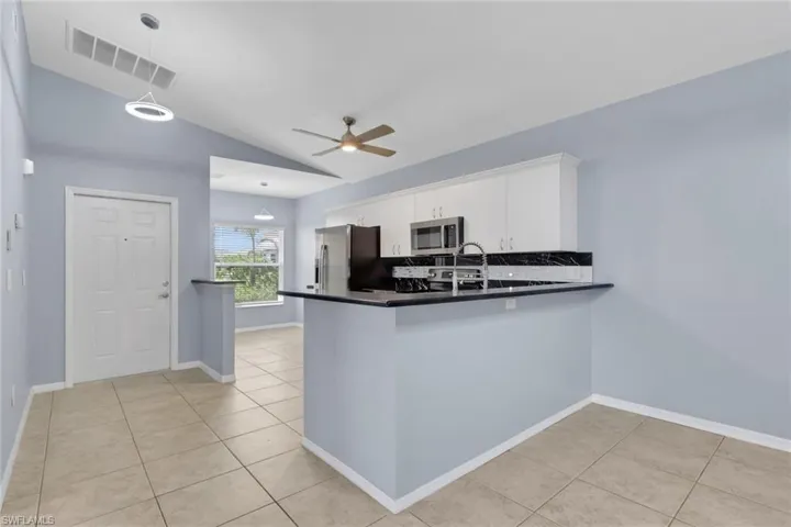 Kitchen featuring white upper cabinetry, stainless steel appliances, black countertops, and a tile backsplash