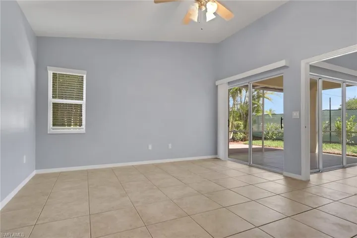 Open concept living area featuring tile flooring, vaulted ceilings, a ceiling fan, and multiple glass sliding doors leading to an outdoor patio