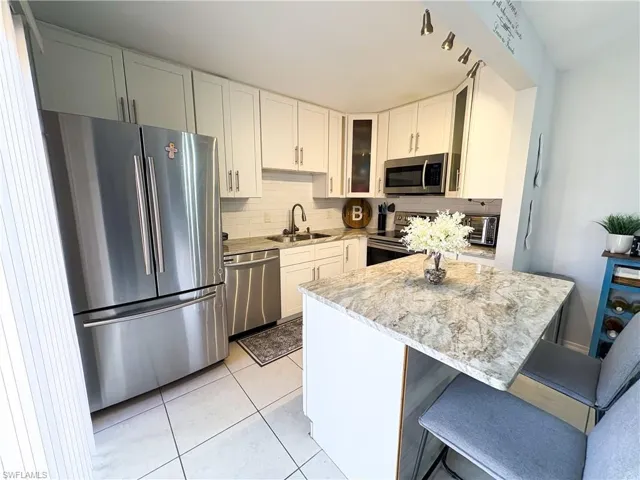 Kitchen with sink, a breakfast bar, stainless steel appliances, light stone countertops, and white cabinets