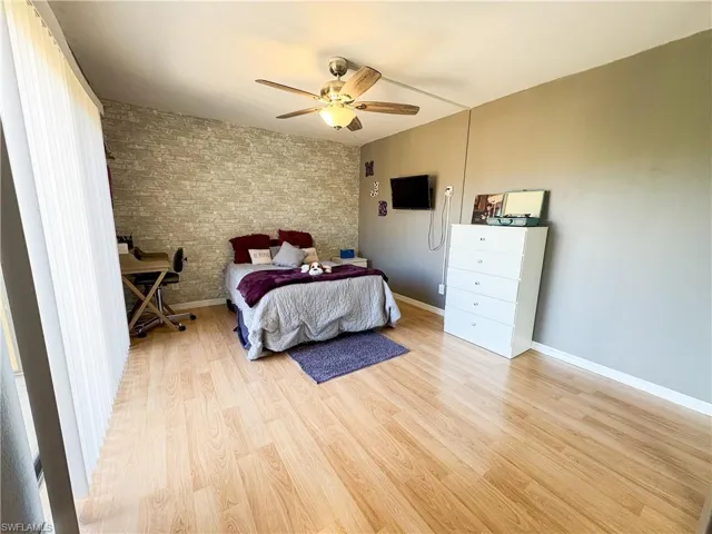 Bedroom featuring ceiling fan, brick wall, and light hardwood / wood-style floors