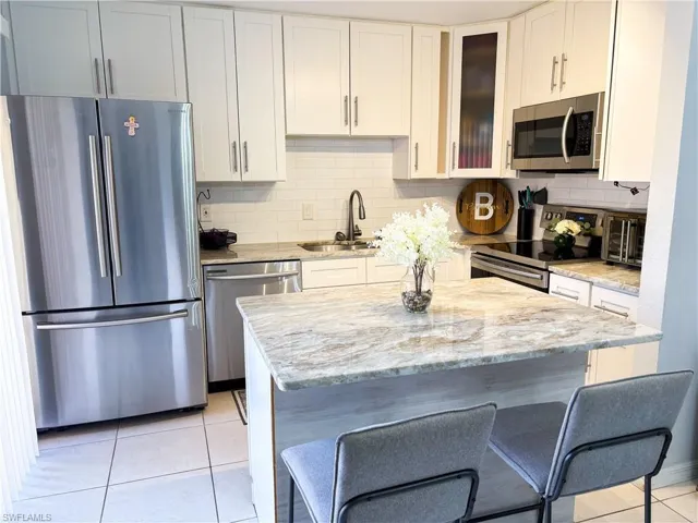 Kitchen featuring light tile patterned floors, sink, stainless steel appliances, light stone countertops, and white cabinets