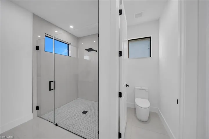 Walk-in shower featuring a glass enclosure, matte black rainfall showerhead, and hexagonal floor tile, paired with a dual-flush toilet and large-format tile flooring