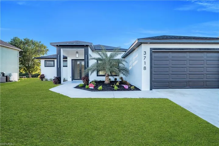 Contemporary single-story exterior featuring a high-contrast white and dark gray facade, a recessed entryway, a multi-panel garage door, and a manicured lawn