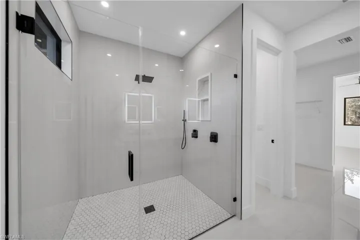 Walk-in shower featuring a glass enclosure, matte black fixtures, integrated storage niche, and hexagonal floor tile