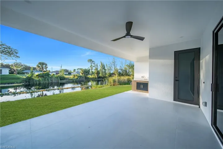 Covered patio featuring large-format tile flooring, built-in outdoor cabinetry, a ceiling fan, and frosted glass door