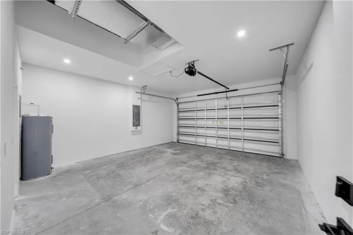 Finished garage featuring smooth-textured walls, recessed lighting, a sectional metal garage door, and a dedicated water heater