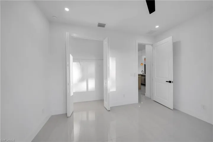 Neutral-toned tile flooring, recessed ceiling lighting, matte black door hardware, and a closet with bifold doors
