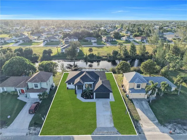 Aerial perspective of a single-story residence featuring a dark shingle roof, concrete driveway, and direct water frontage